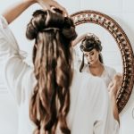 Kobieta stojąca przed lustrem i układająca sobie fryzurę