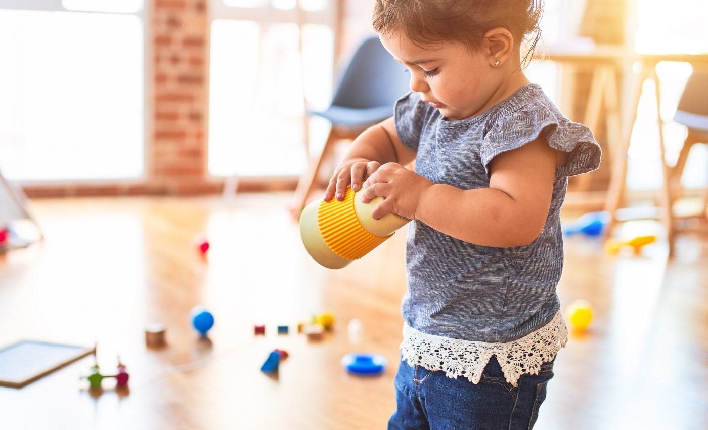 Dziecko w pokoju pełnym zabawek trzyma w dłoniach żółtą zabawkę