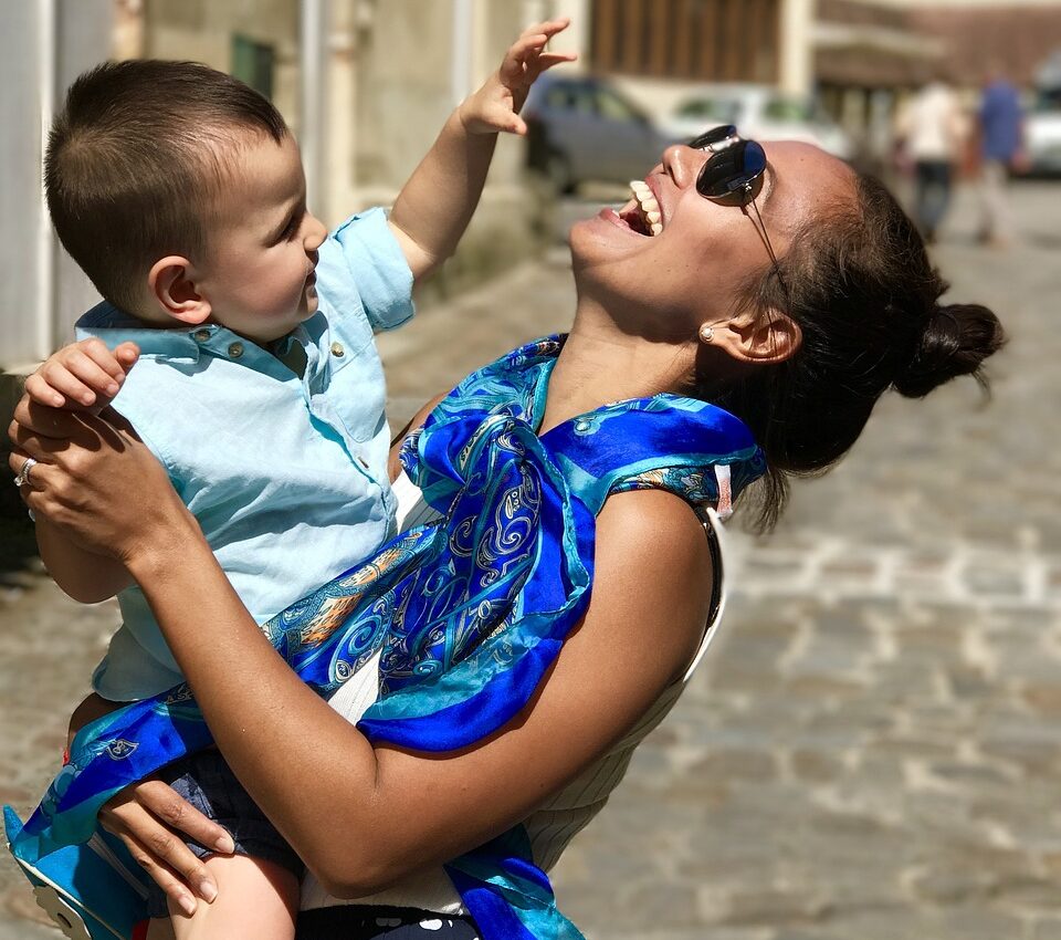 Roześmiana kobieta w niebieskiej chustce trzyma dziecko