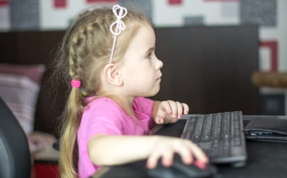 Mała dziewczynka w różowej bluzce korzystająca z komputera