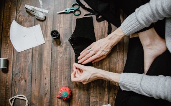 Kobieta siedząca na podłodze i szyjąca lub naprawiająca ubranie