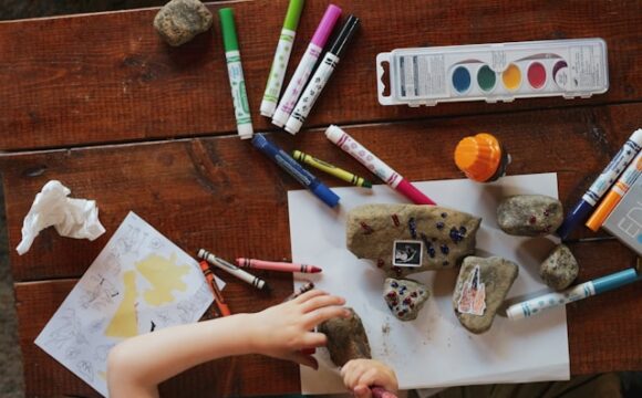 drewniany stół z mazakami, farbkami i kamykami będące dodatkowymi zajęciami dla dziecka