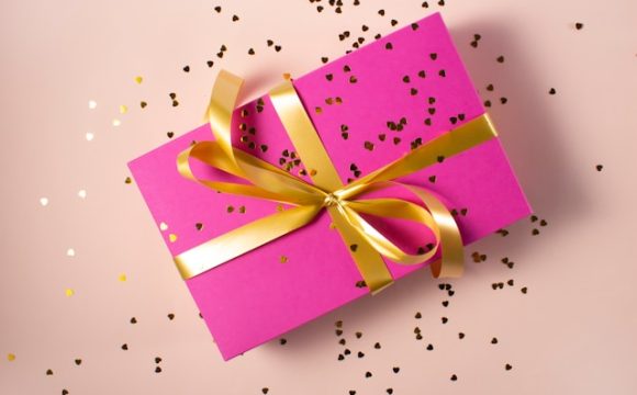 Prezent opakowany w różowy papier i obwiązany złotą wstążką