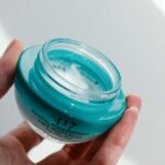Dłoń trzymająca niebieski szklany pojemnik z kremem do twarzy