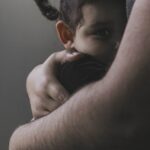 Smutny chłopiec szukający wsparcia w ramionach dorosłego