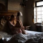 Kobieta w białej sukience siedząca na niezasłanym łóżku