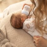 Niemowlak leżący na poduszce, który jest karmiący butelką