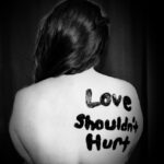 Napis love shouldn't hurt namalowany na plecach kobiety