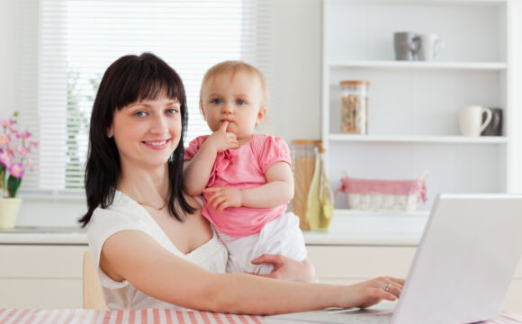 Kobieta trzymająca dziecko na kolanach jednocześnie pracująca na laptopie