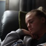 Kobieta w szarej bluzie leży na sofie i odpoczywa