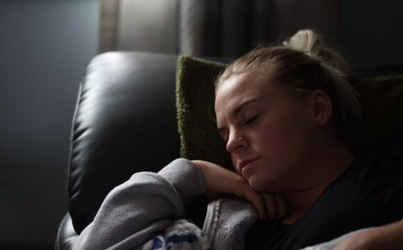 Kobieta w szarej bluzie leży na sofie i odpoczywa