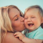 Matka trzymająca na rękach i całująca dziecko ubrane w niebieską koszulkę