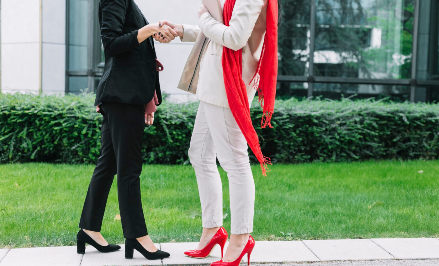Dwie rozmawiające kobiety jedna ubrana w czarny strój i ma czarne buty, a druga w białym stroju i ma czerwone butach