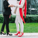 Dwie rozmawiające kobiety jedna ubrana w czarny strój i ma czarne buty, a druga w białym stroju i ma czerwone butach