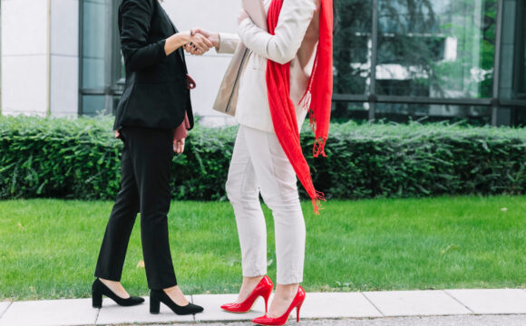 Dwie rozmawiające kobiety jedna ubrana w czarny strój i ma czarne buty, a druga w białym stroju i ma czerwone butach