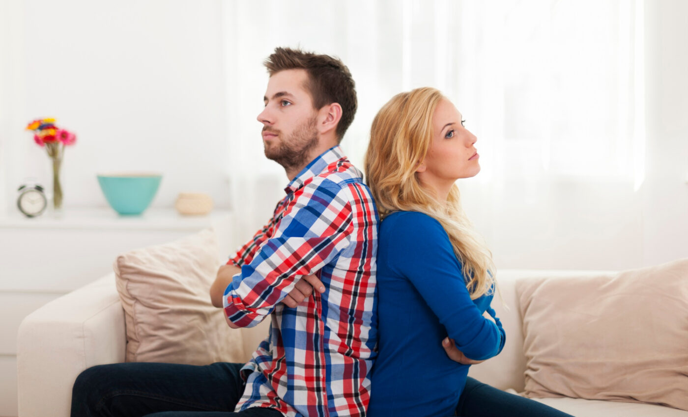 Kobieta w niebieskiej bluzce i mężczyzna w koszuli w kratkę siedzą z założonymi rękoma i są odwróceni do siebie plecami