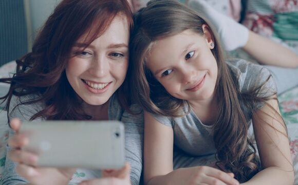 Matka z córką leży na łóżku i robi wspólne zdjęcie